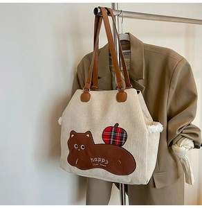 Detail of corduroy tote bag featuring animal embroidery and brown leather handles