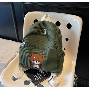 Detail of dark green corduroy backpack with cute cartoon bear embroidery on white chair