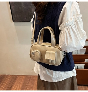 Beige multi-pocket bowling bag worn with navy vest and white shirt in a minimal interior