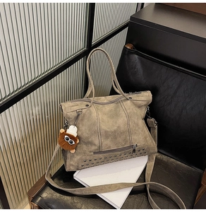 Macro detail of dark khaki tote bag with rivet accents and plush monster charm