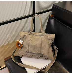 Detail view of khaki rivet tote bag with fringe and plush pendant on black leather chair