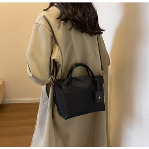 Detail of a black nylon tote bag with leather straps on a beige trench coat