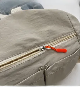 Detail einer beige Nylon Umhängetasche mit Reißverschluss und orangefarbenem Kordelzug