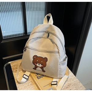 Detail view of cream-colored corduroy backpack with cute bear embroidery on marble surface