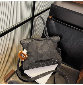 Detail of grey washed leather tote bag with rivets and lion charm on a leather chair