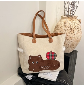 Detail of corduroy tote bag with cat embroidery and leather handles in a cozy setting