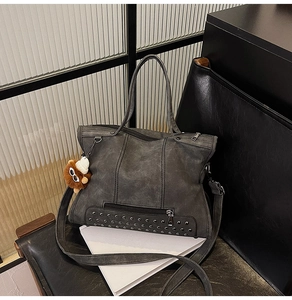 Detail of dark grey tote bag with metal studs and tassel on a leather chair