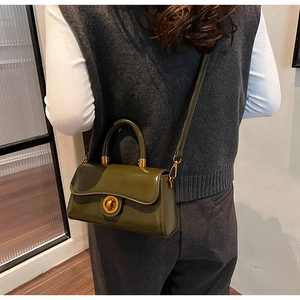 Detail of dark green glossy crossbody bag with golden clasp shown on a model