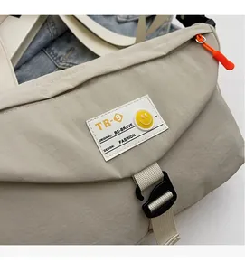 Detail der beigen Nylon-Umhängetasche mit orangefarbenem Zipper und Smiley-Abzeichen