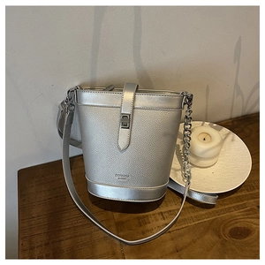 Detail of silver textured bucket bag with metal twist lock and chain strap on wooden table