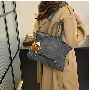 Detail of dark grey vintage tote bag with rivet base and plush charm on trench coat