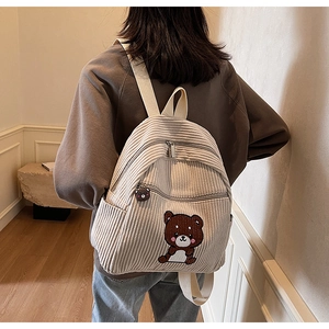 Detail of white corduroy backpack showing cute bear patch and plush charm on woman back