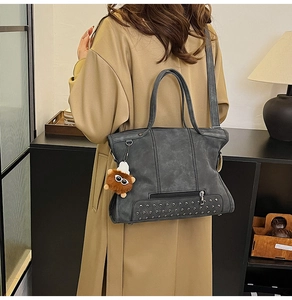 Detail of dark grey rivet handbag with plush charm and long coat outfit styling