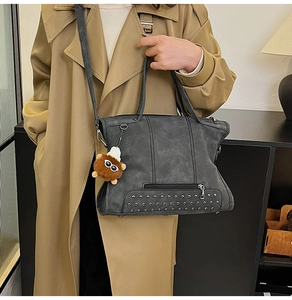 Detailed view of dark grey tote bag with silver rivets and plush doll accessory