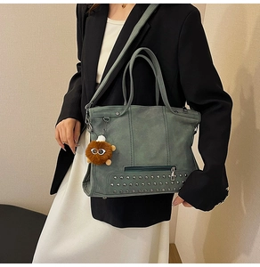 Detail of dark green vintage tote bag with rivets and plush pendant shown on shoulder