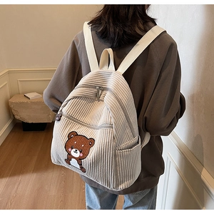 Detail of beige corduroy backpack featuring a cute brown cartoon bear embroidery
