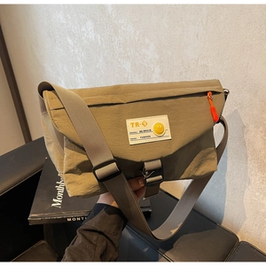 Detail der khakifarbene Kuriertasche mit weißem Logo-Patch und orangem Reißverschluss