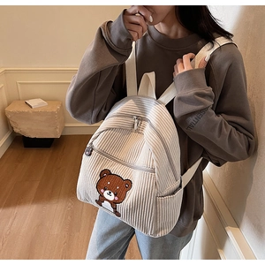 Detail of light beige corduroy backpack with brown bear patch and cartoon zipper pulls