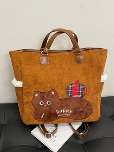 Brown corduroy tote bag with cat embroidery and lamb wool trim on a black leather sofa