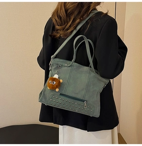 Gray-green tote bag with studs and plush charm shown on person wearing a black blazer