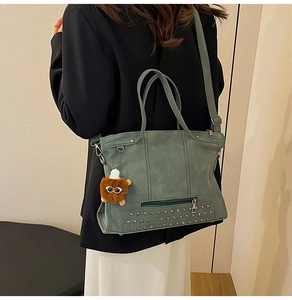 Close-up of green tote bag with silver studs and a decorative plush charm detail