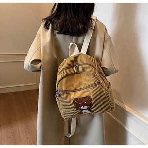 Detailed texture of yellow corduroy backpack featuring a cute brown bear embroidery