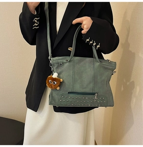 Detail of green faux leather tote bag with silver metal rivets and fluffy doll pendant