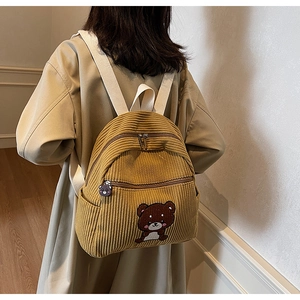 Detail showing ginger yellow corduroy backpack with cute bear embroidery on model