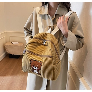 Close-up of mustard yellow corduroy backpack with cute bear embroidery and cream straps