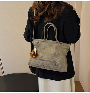 Detail of grey-green fringe bag with metallic rivets and a cute brown plush pendant