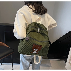Detailed close-up of dark green corduroy backpack texture with cute bear embroidery