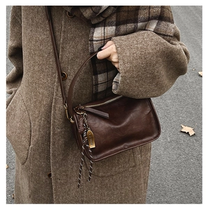 Détail du sac à bandoulière en cuir marron foncé avec logo doré et pendentif tissé