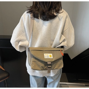 Makroaufnahme der khakifarbenen Kuriertasche mit weißem Webetikett und orangem Reißverschluss