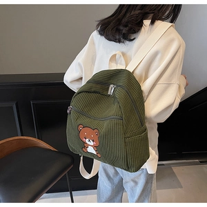 Detail of dark green corduroy backpack featuring a cute cartoon bear embroidery on back
