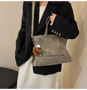 Macro detail of olive green suede tote bag featuring silver studs and plush doll charm