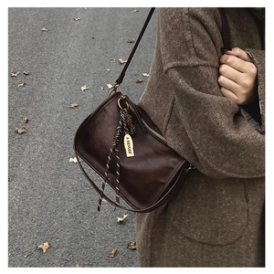 Détail d'un sac à bandoulière en cuir marron foncé avec logo doré et charme tissé