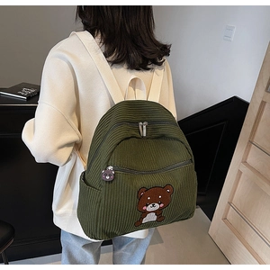 Detail of green corduroy backpack showing a brown bear patch and side pocket for umbrella