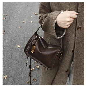 Détail d'un sac bandoulière en cuir marron avec plaque logo dorée et breloque tressée
