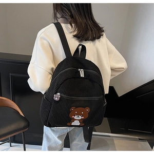 Detail of black corduroy backpack featuring a cute brown bear embroidery and charm