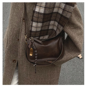 Détail du sac bandoulière marron foncé avec boucles dorées et pendentif sur manteau en tweed