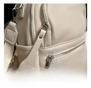 Macro shot of silver zippers and litchi grain leather texture on a beige backpack