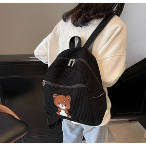 Detail of black corduroy backpack with cute bear embroidery shown on a female model
