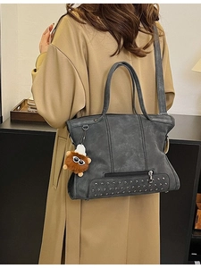 Dark grey tote bag with metal rivets and plush monster charm shown on model shoulder