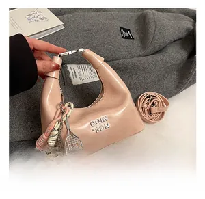 Détail du sac à main croissant rose clair avec logo métallique et breloque raquette tennis
