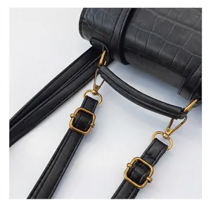 Detail of adjustable strap with bronze metal buckle on black crocodile textured bag