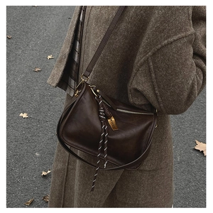 Détail du sac bandoulière marron foncé avec cordon tressé et logo sur métal doré