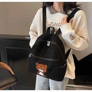Detail of black corduroy backpack featuring a cute brown bear embroidery and zippers