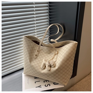 Close-up of cream monogram tote bag with chic dog-shaped charm on a minimalist desk