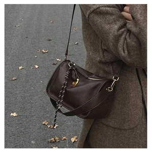 Détail d'un sac bandoulière en cuir marron foncé avec finitions dorées et breloque tressée