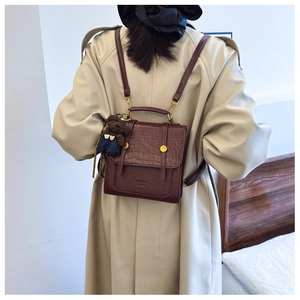 Detail of dark brown faux crocodile texture backpack with a cute plush bear charm
